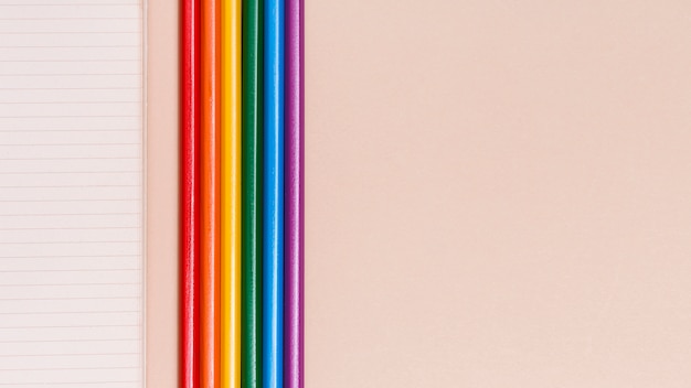 Bunte Bleistifte und Notizbuch des Regenbogens auf beige Hintergrund