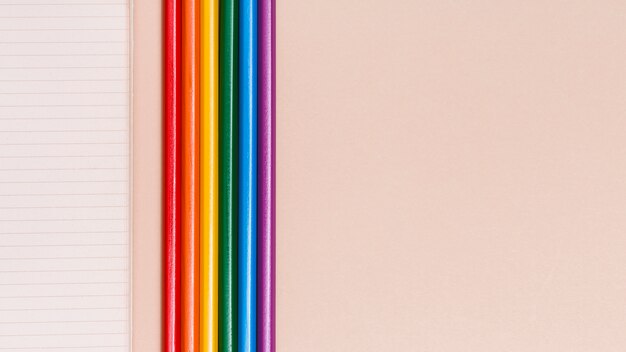 Bunte Bleistifte und Notizbuch des Regenbogens auf beige Hintergrund