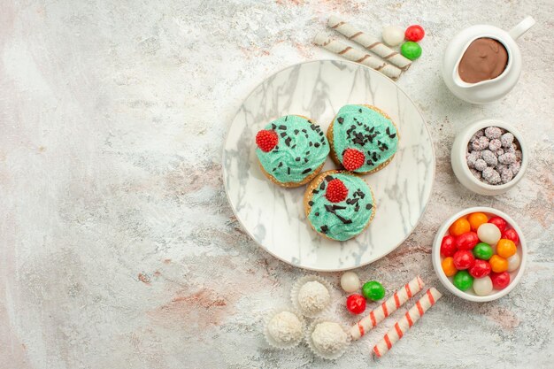 Bunte Bonbons der Draufsicht mit cremigen Kuchen auf weißer Oberflächenfarbe Regenbogen-Keks-Tee-Kuchen