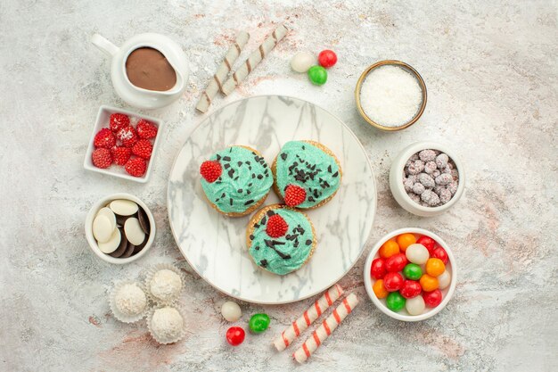 Bunte Bonbons der Draufsicht mit Sahnetorten auf weißem Oberflächenkeks süßem Kuchenteeplätzchen