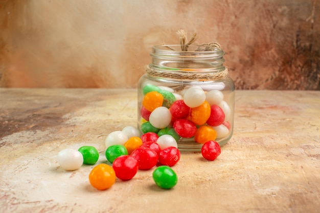 Kostenloses Foto bunte bonbons der vorderansicht innerhalb der glasdose auf hellem hintergrund