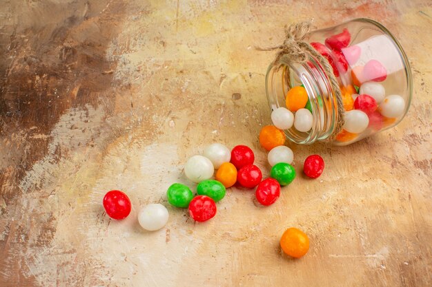 Bunte Bonbons der Vorderansicht innerhalb der Glasdose auf hellem Hintergrund