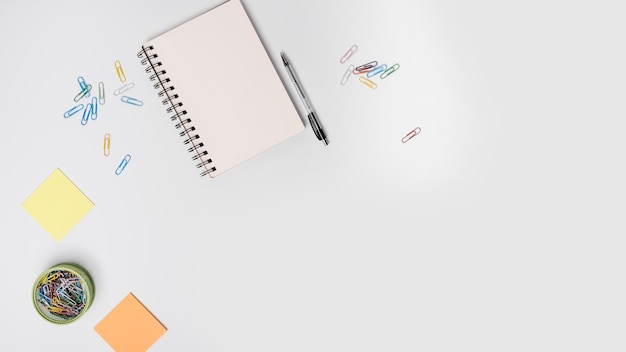 Bunte Büroklammern; Spiralblock; Stift; Haftnotiz auf weißem Hintergrund