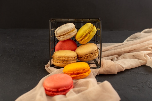 Bunte französische Macarons der Vorderansicht, die köstlich und im Korb auf der dunklen Oberfläche gebacken werden