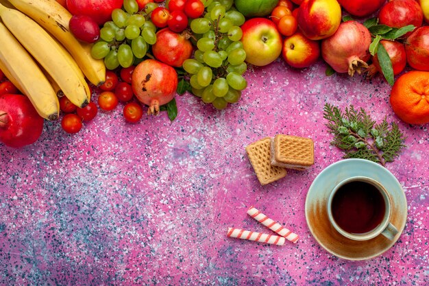 Bunte Früchte der Frischobstzusammensetzung der Draufsicht mit Tee auf hellrosa Oberfläche