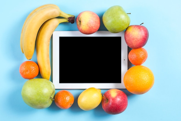 Bunte Früchte umgeben mit digitaler Tablette auf blauem Hintergrund