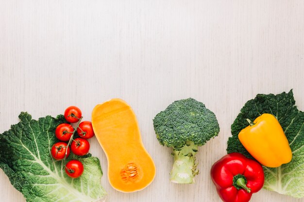 Bunte Kirschtomaten; halbierter Butternusskürbis; Paprika- und Kohlblatt auf hölzernem Schreibtisch