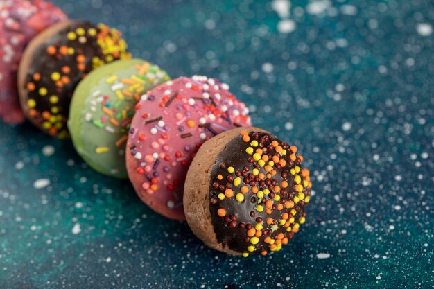 Bunte kleine Donuts mit Streuseln auf einer blauen Oberfläche.