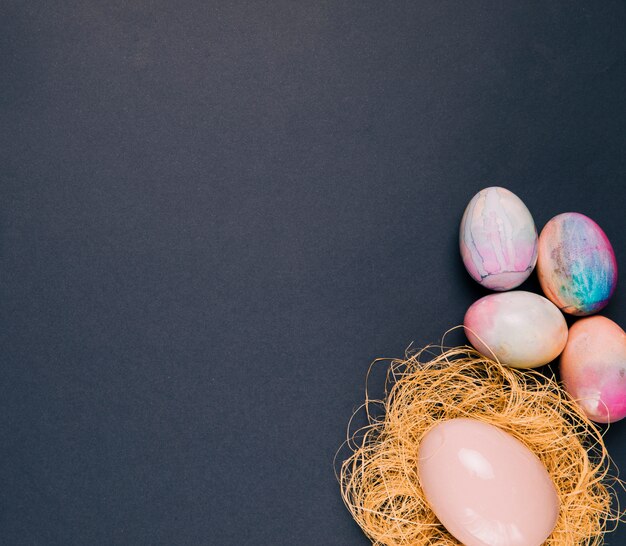 Bunte Ostereier und rosafarbenes Ei auf dem Nest über der Ecke des schwarzen Hintergrundes