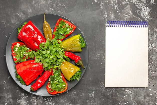 Bunte Pfefferteller der oberen Nahaufnahmeansicht der Paprika mit Kräutern neben dem weißen Notizbuch