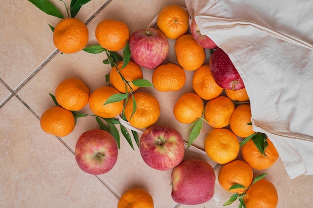 Kostenloses Foto bunte reife früchte in einer wiederverwendbaren öko-tüte auf einem fliesenboden lieferung von mandarinen und äpfeln gesunde ernährung vitamine blick von oben