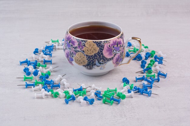 Bunte Reißnägel und eine Tasse Tee auf weißer Oberfläche