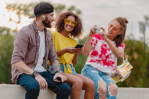 Bunte stilvolle glückliche junge Gesellschaft der Freunde, die Park sitzen