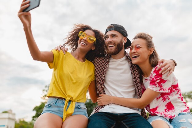 Bunte stilvolle glückliche junge Gesellschaft der Freunde, die Park sitzen