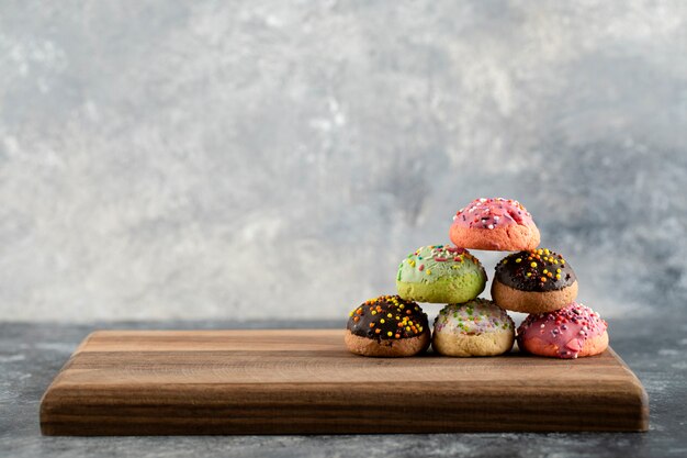 Bunte süße Donuts mit Streuseln auf einem hölzernen Schneidebrett.