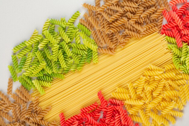 Bunte ungekochte Spiralnudeln und Spaghetti auf weißer Oberfläche