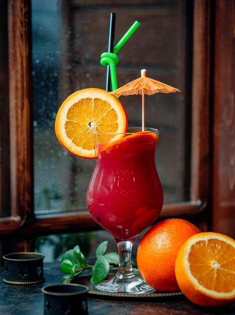 bunter Cocktail mit Orangenscheibe, Cocktailschirm, grünem und schwarzem Stroh