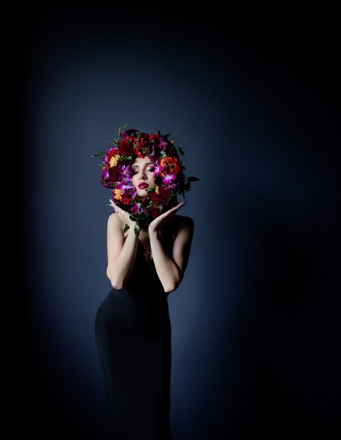 Bunter Kreis gemacht von den frischen Blumen auf dem Gesicht des schönen Mädchens, Frau gekleidet in schwarzem engem Kleid auf dem dunkelblauen Hintergrund