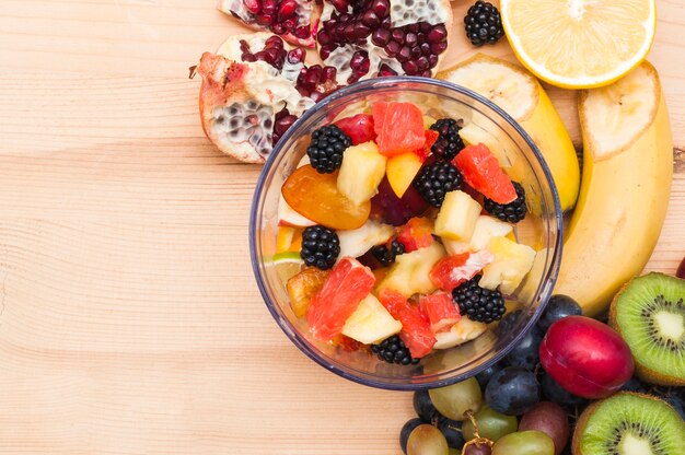 Bunter Obstsalat in der Glasschüssel auf hölzernem Schreibtisch