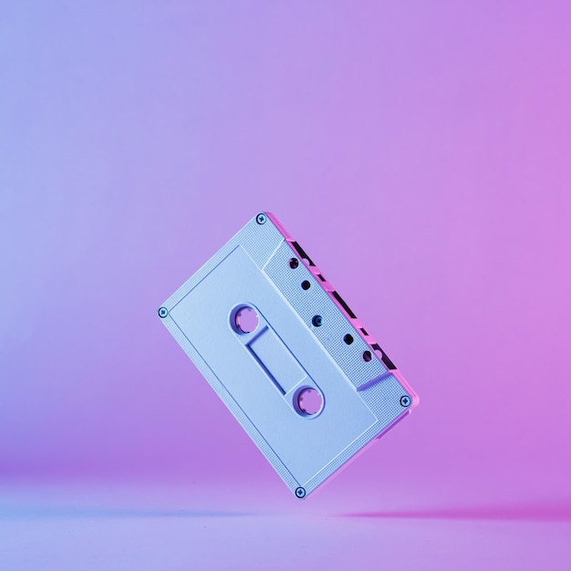 Buntes künstlerisches stillleben einer alten audiokassette, die im rand über einem abgestuften violetten hintergrund balanciert Premium Fotos