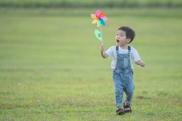 Buntes Windmühlenspielzeug für Kinder. lachendes Kind, das glücklich spielt. Kleiner Junge bläst im Sommer im Sommerlager in der Sonne gegen eine bunte Windmühle.