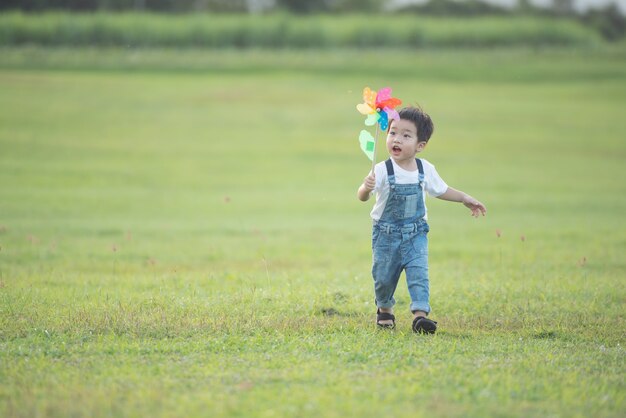 Buntes Windmühlenspielzeug für Kinder. lachendes Kind, das glücklich spielt. Kleiner Junge bläst im Sommer im Sommerlager in der Sonne gegen eine bunte Windmühle.