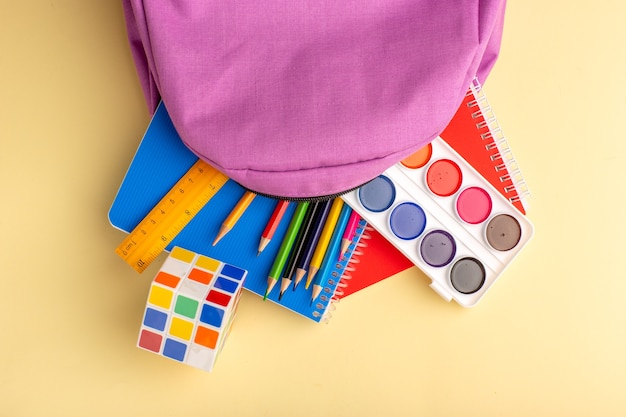 Buntstifte der Draufsicht mit Copybook-Farben und lila Tasche auf hellgelbem Schreibtisch Schulfilzstift-Bleistiftbuch-Notizblock