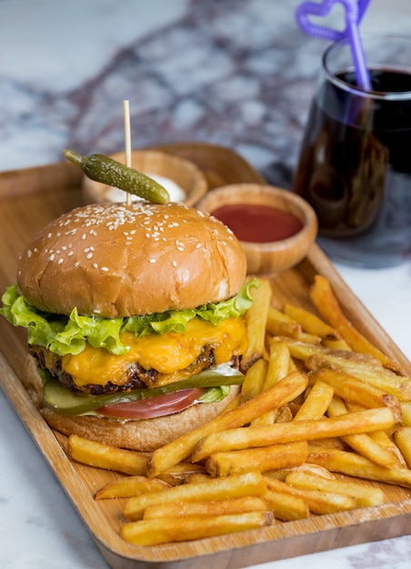 Burger mit Pommes und rotem Getränk innerhalb der hölzernen Servierplatte.