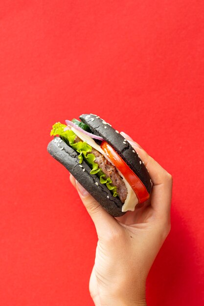 Burger mit schwarzem Brötchen auf rotem Hintergrund