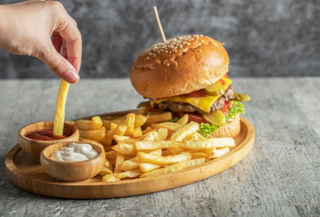 Burger und Bratkartoffeln auf einer Holzplatte mit Saucen