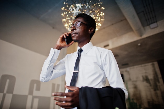Business-Afroamerikaner trägt weißes Hemd, Krawatte und Brille im Büro und spricht am Handy