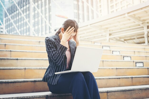 Business-Frau betont, während mit Laptop sitzt auf den Stufen. Geschäftsleute Konzept.