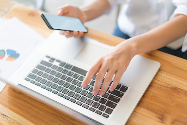 Business-Frau Hand mit finanziellen Charts und Handy über Laptop auf dem Tisch.