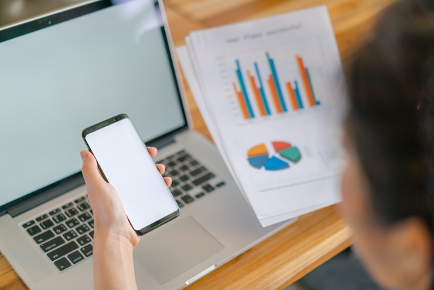 Business-Frau Hand mit finanziellen Charts und Handy über Laptop auf dem Tisch.