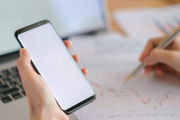 Business-Frau Hand mit finanziellen Charts und Handy über Laptop auf dem Tisch.