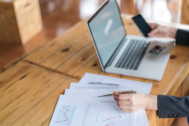 Business-Frau Hand mit finanziellen Charts und Laptop auf dem Tisch.