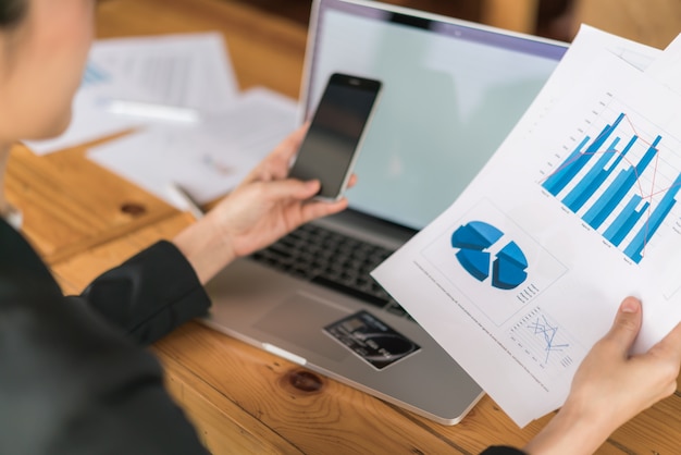 Business-Frau Hand mit finanziellen Charts und Laptop auf dem Tisch.