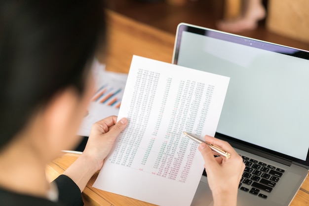 Business-Frau Hand mit finanziellen Charts und Laptop auf dem Tisch.