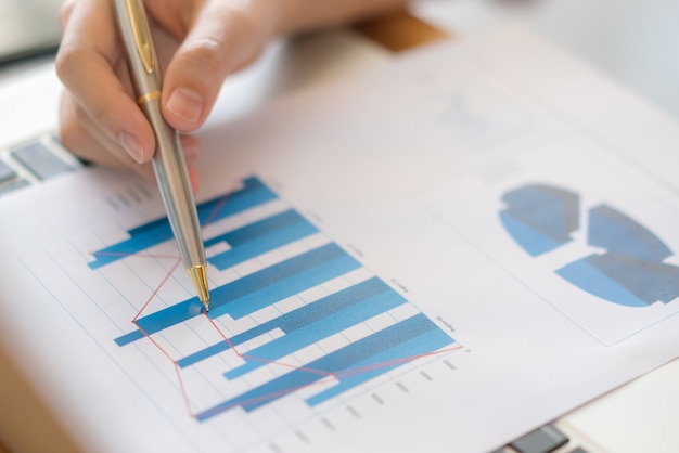 Business-Frau Hand mit finanziellen Charts und Laptop auf dem Tisch.