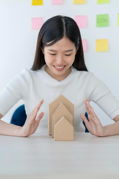 Business Home Asset Ideen Konzept mit schöner, intelligenter asiatischer Frau Hand schützt Hausmodell mit Glück und Selbstvertrauen