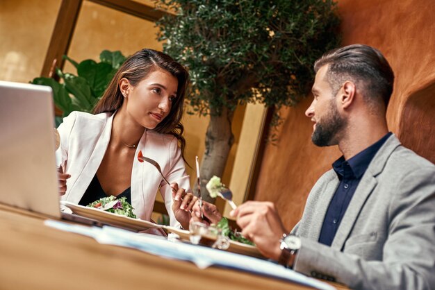 Business-lunch-mann und frau sitzen am tisch im restaurant und essen gesunden frischen salat diskutieren