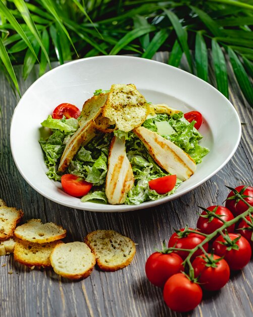 Caesar Salat mit Huhn und Kirschtomaten in einem weißen Teller auf einem Holztisch