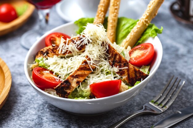 Caesar-Salat von der Seite mit gegrilltem Hühnchen-Parmesan-Tomatensalat und Brotstangen