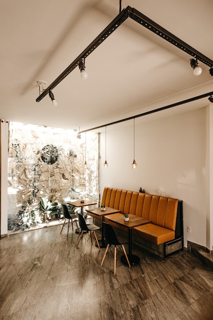 Cafe Interieur mit einem orangefarbenen Sofa, drei Tischen und drei schwarzen Stühlen