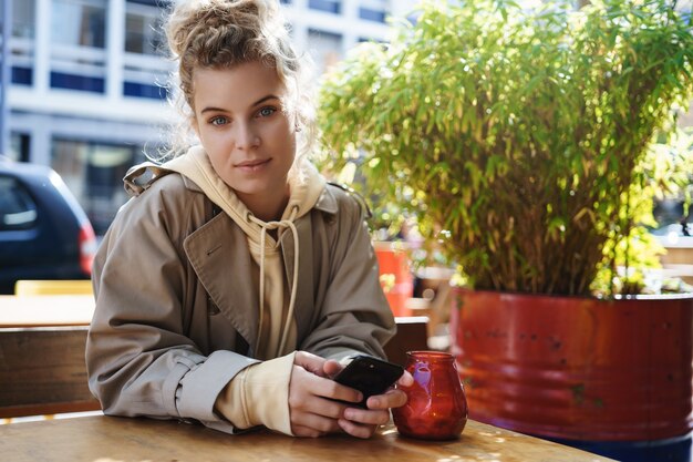 Café-Klientin der jungen Frau, die draußen sitzt und ein Mobiltelefon benutzt.