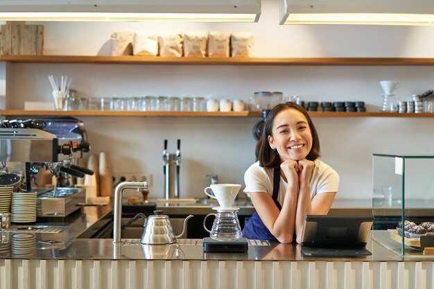 Café und Kleinunternehmen lächelnder asiatischer Barista in Schürze, der hinter der Theke im Café arbeitet