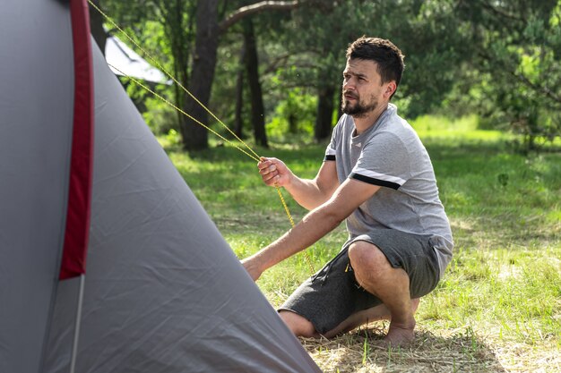 Camping, Reisen, Tourismus, Wanderkonzept - junger Mann, der ein Zelt im Wald aufstellt.