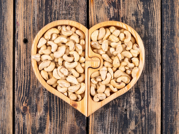 Cashew in einer herzförmigen Holzteller-Draufsicht auf einem Holztisch