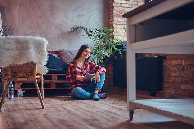 Charmante Brünette in einem Flanellhemd und Jeans sitzt auf einem Flohnetzwerk