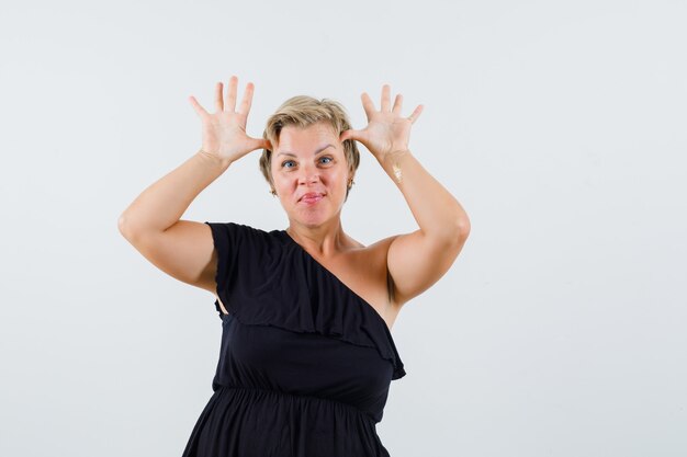 Charmante Dame, die Stierhorn über ihrem Kopf in der schwarzen Bluse zeigt und verspielt aussieht